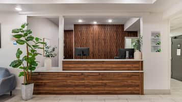 A reception desk with a wooden panel backdrop, a computer, and a plant.