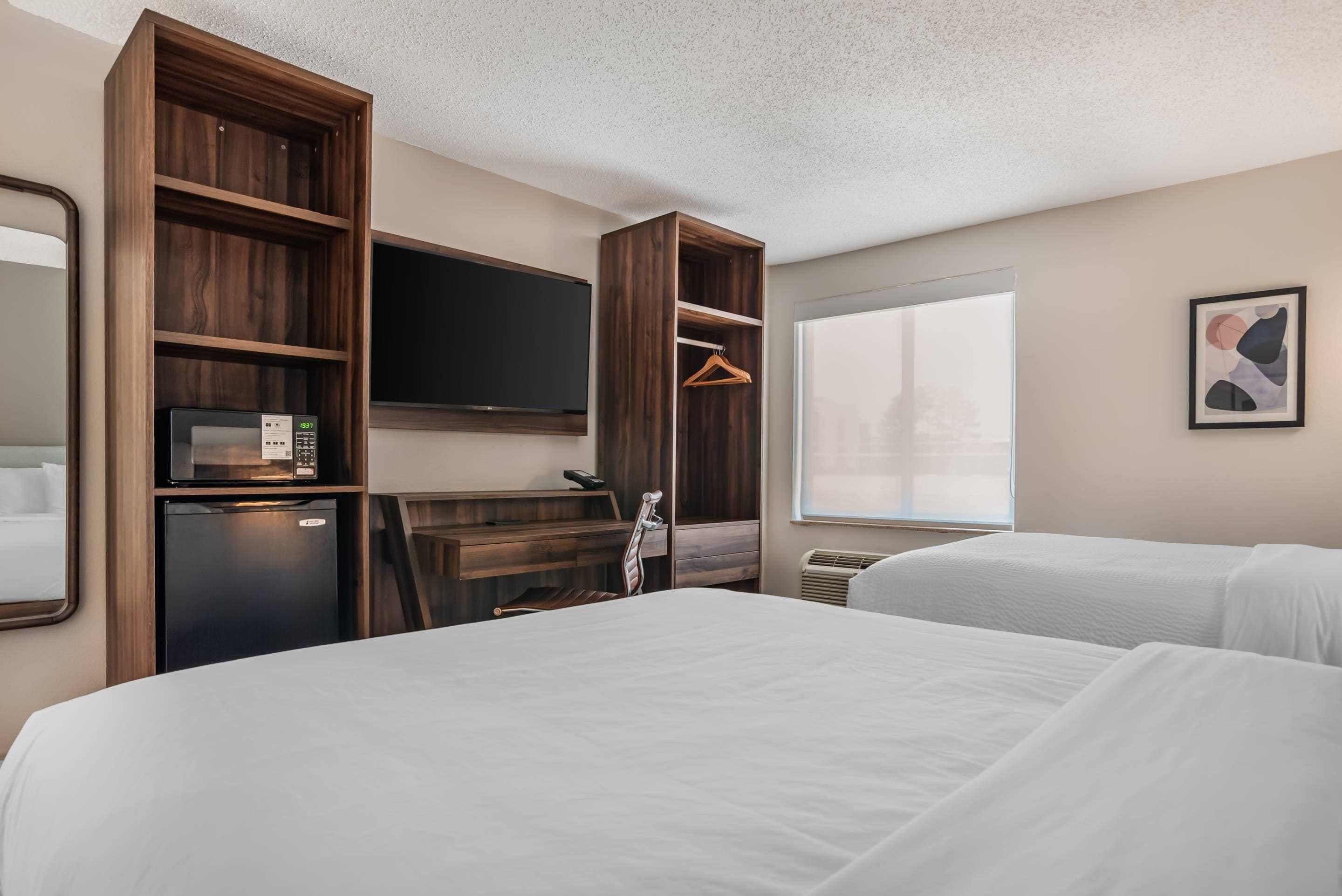 A hotel room with a bed, a desk with a computer, a television, and a window.
