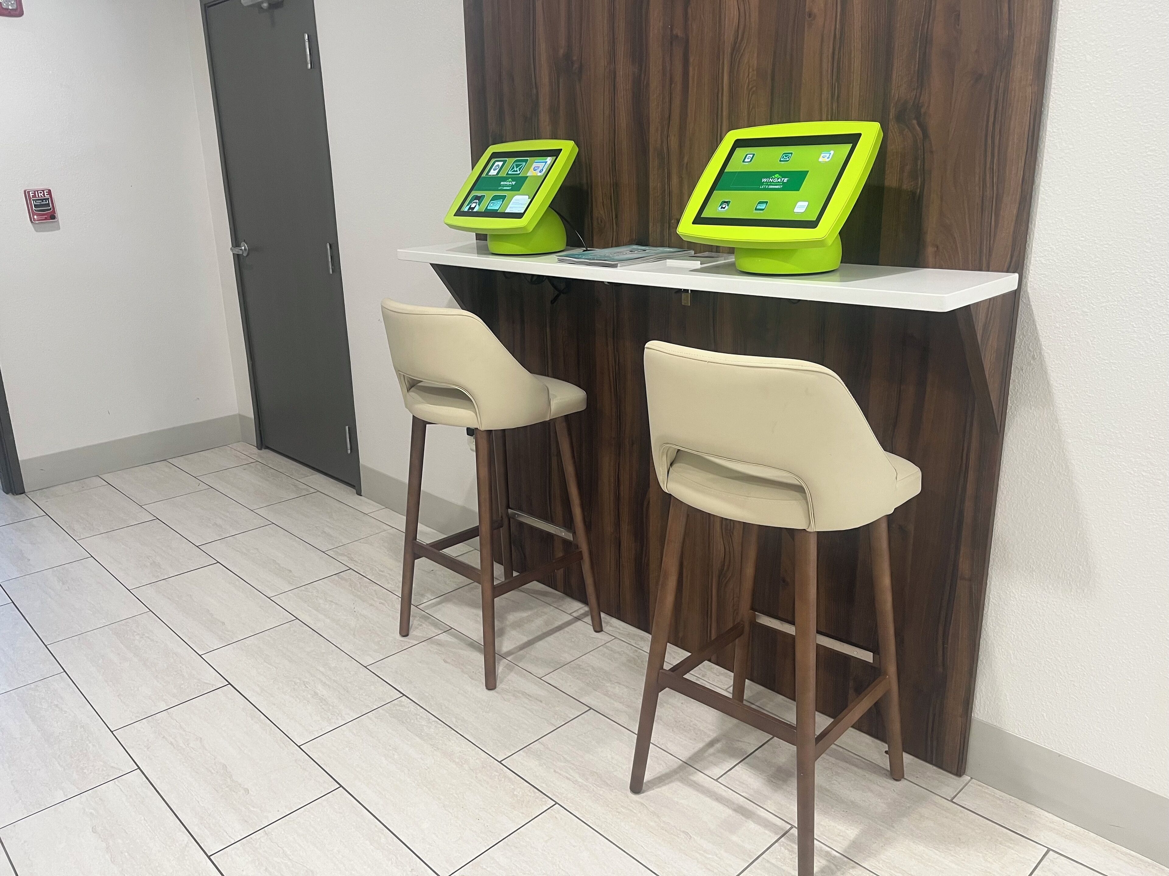 A reception area with two bar stools and a counter with two green digital kiosks.