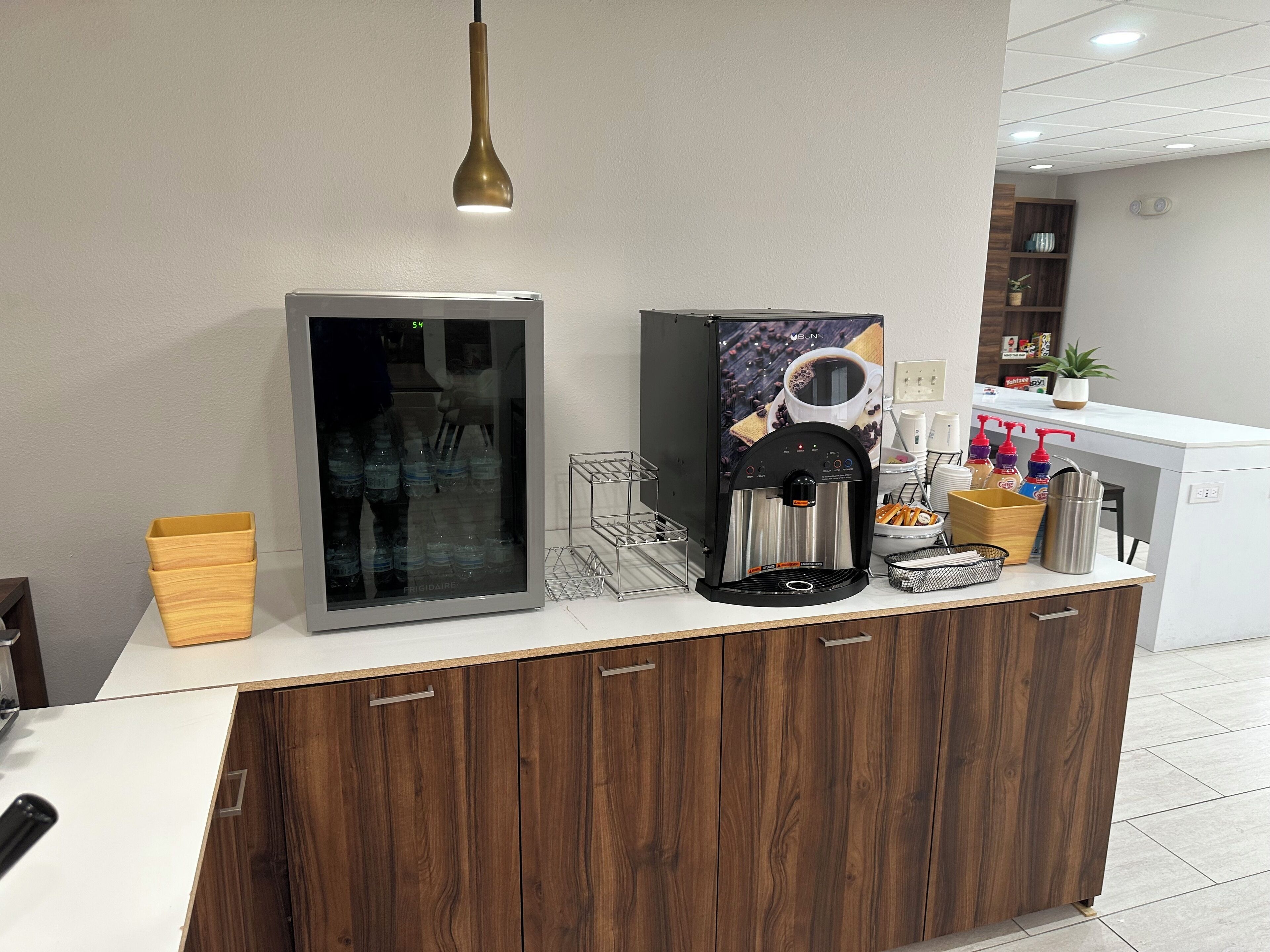 A modern kitchen area with a coffee machine, a refrigerator, and a wooden cabinet.