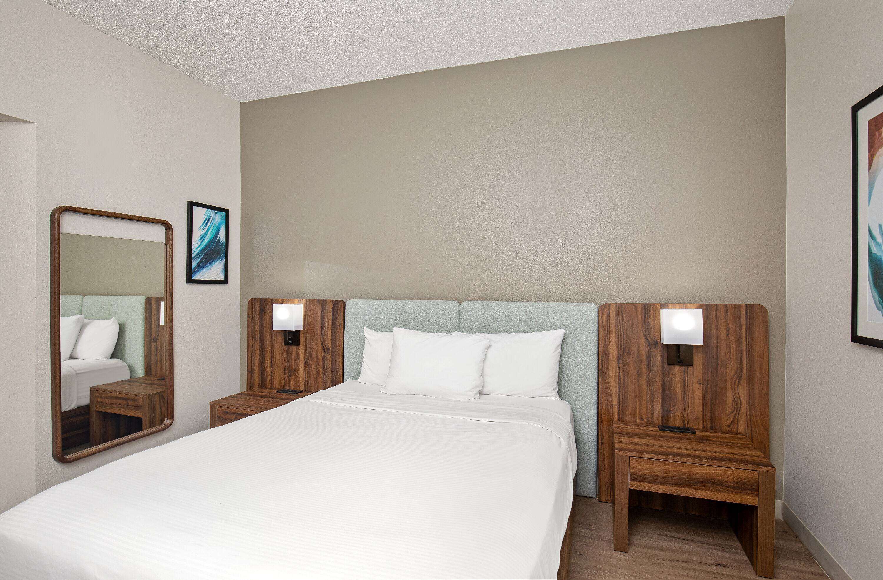 A hotel room with a large bed, wooden headboard, two bedside tables with lamps, and a mirror.
