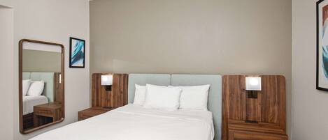 A hotel room with a large bed, wooden headboard, two bedside tables with lamps, and a mirror.