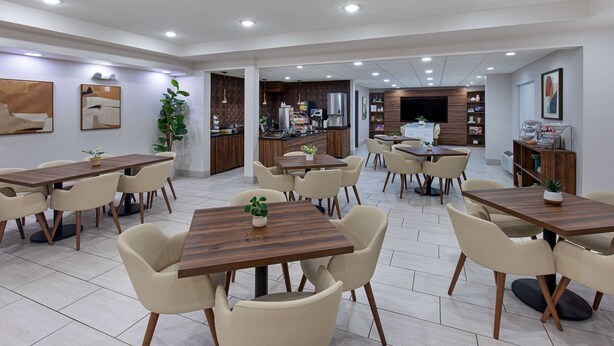 A spacious dining area with multiple tables and chairs, a kitchen in the background, and artwork on the walls. - Wingate by Wyndham Hattiesburg (Hattiesburg)