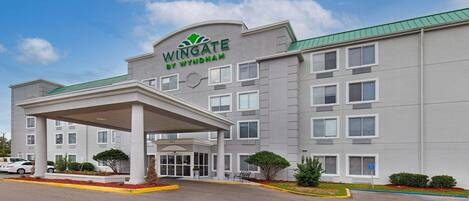 A Wingate by Wyndham hotel with a covered entrance, multiple windows, and a green roof.