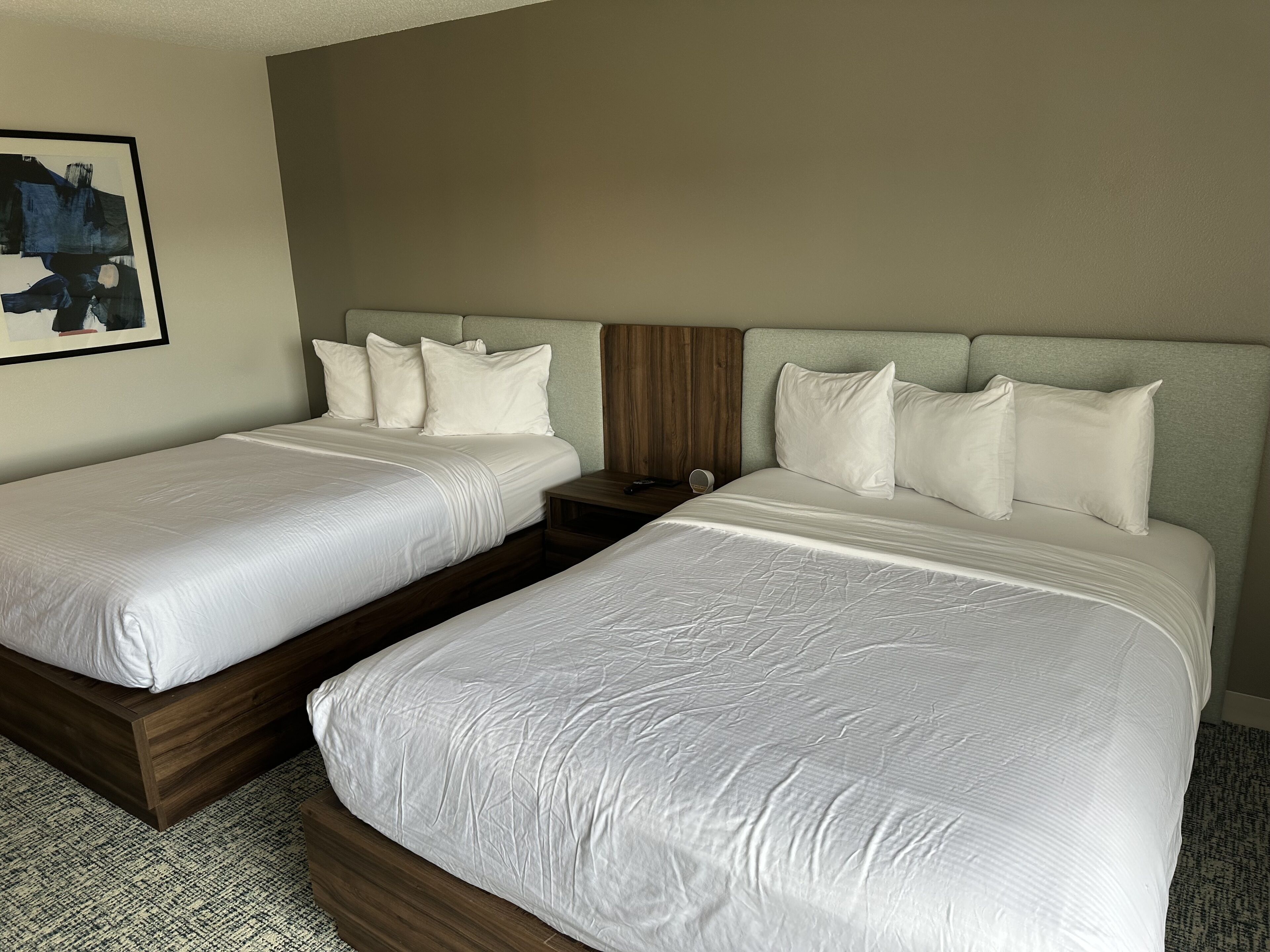 Habitación de hotel con dos camas, cada una con sábanas blancas y cabeceros de madera.