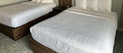 Habitación de hotel con dos camas, cada una con sábanas blancas y cabeceros de madera.