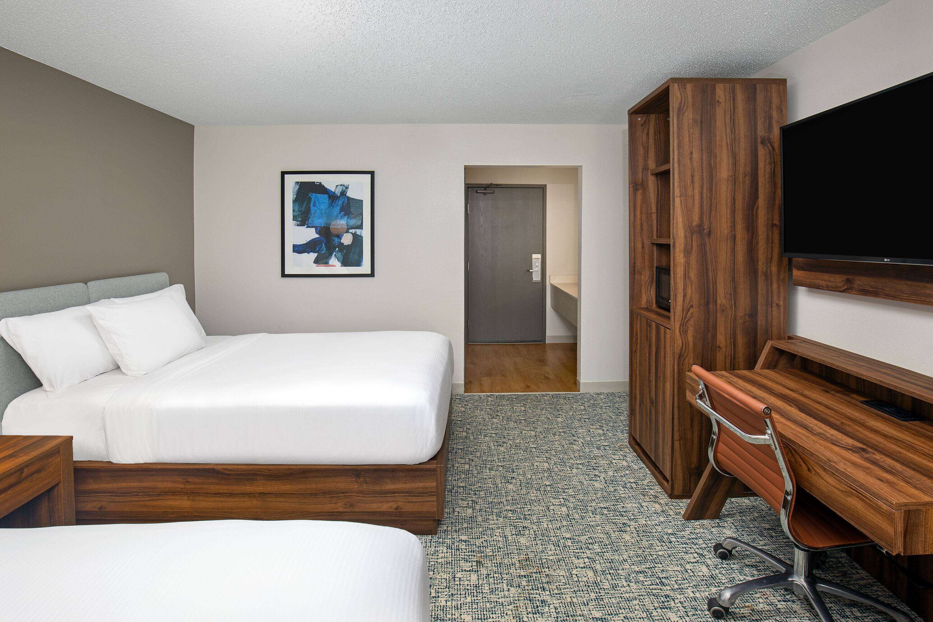 A hotel room with a bed, a desk, a chair, a television, and a framed picture on the wall.