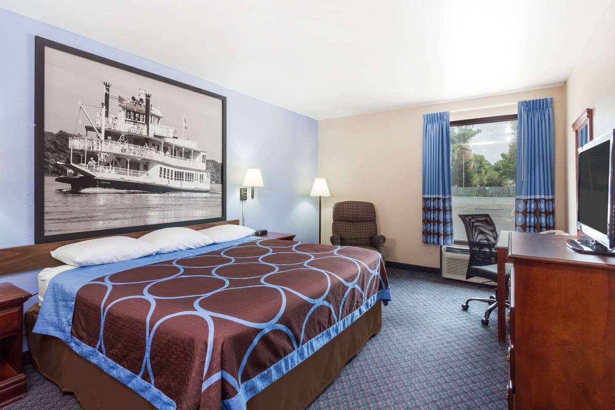 Habitación de hotel con una cama grande, un escritorio, una silla, un televisor y una ventana con cortinas.