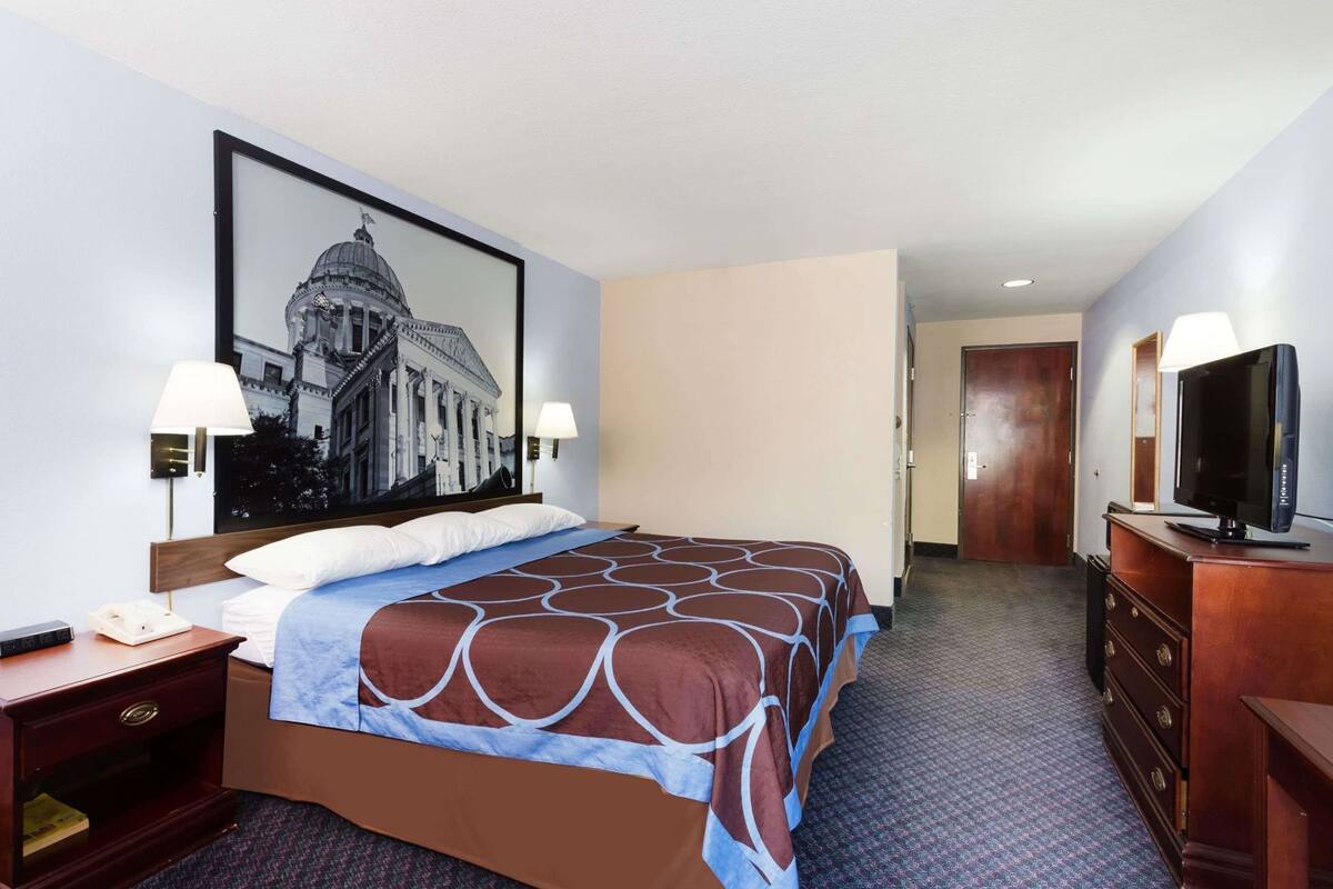 Habitación de hotel con una cama grande, un televisor, un escritorio con lámpara y un cuadro en la pared.