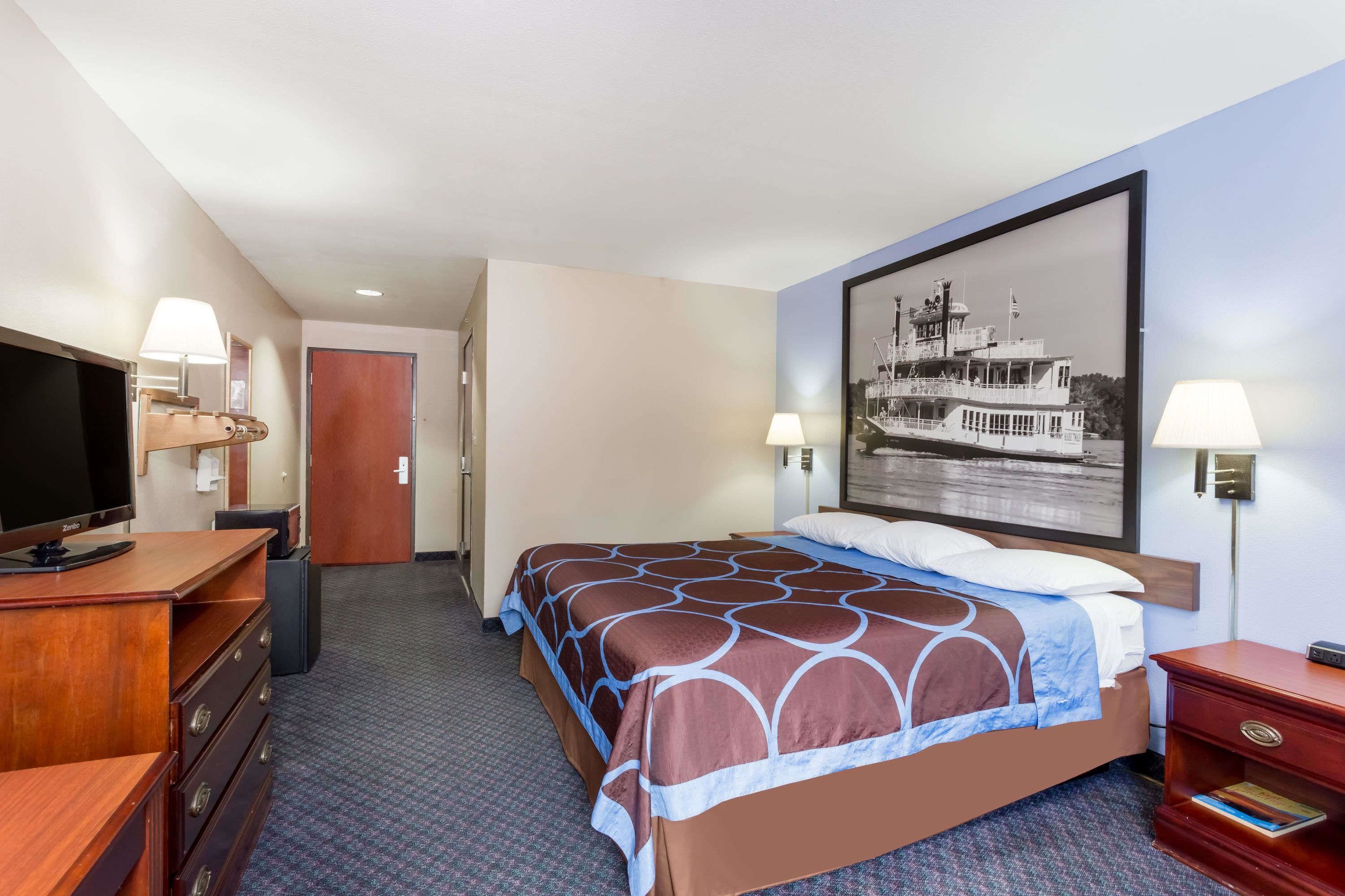Una habitación de hotel con cama, televisor, escritorio y un cuadro en la pared.