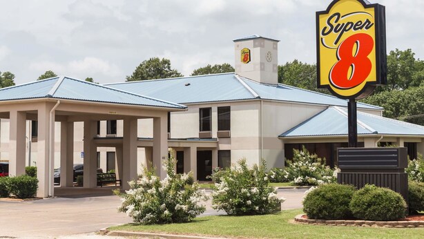 Un hotel Super 8 con un letrero grande, estacionamiento techado y jardines bien cuidados.