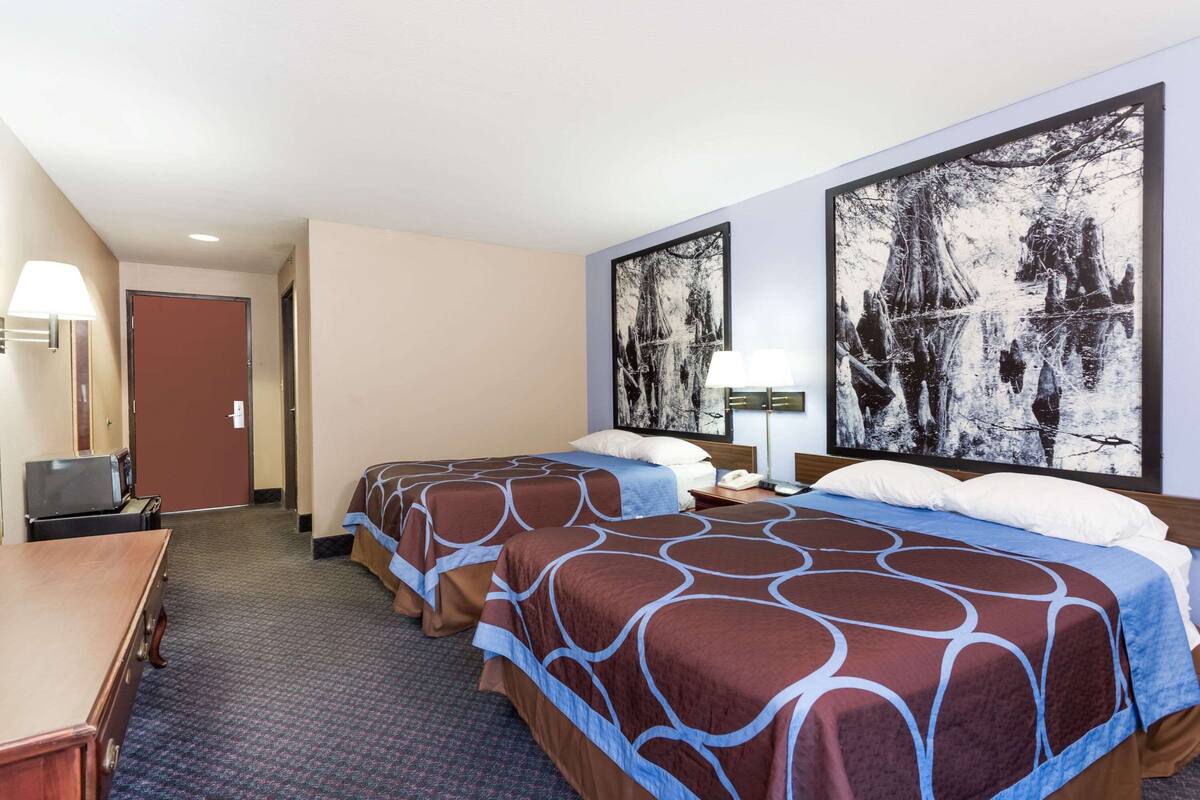 Habitación de hotel con dos camas, un escritorio, un televisor y obras de arte en las paredes.