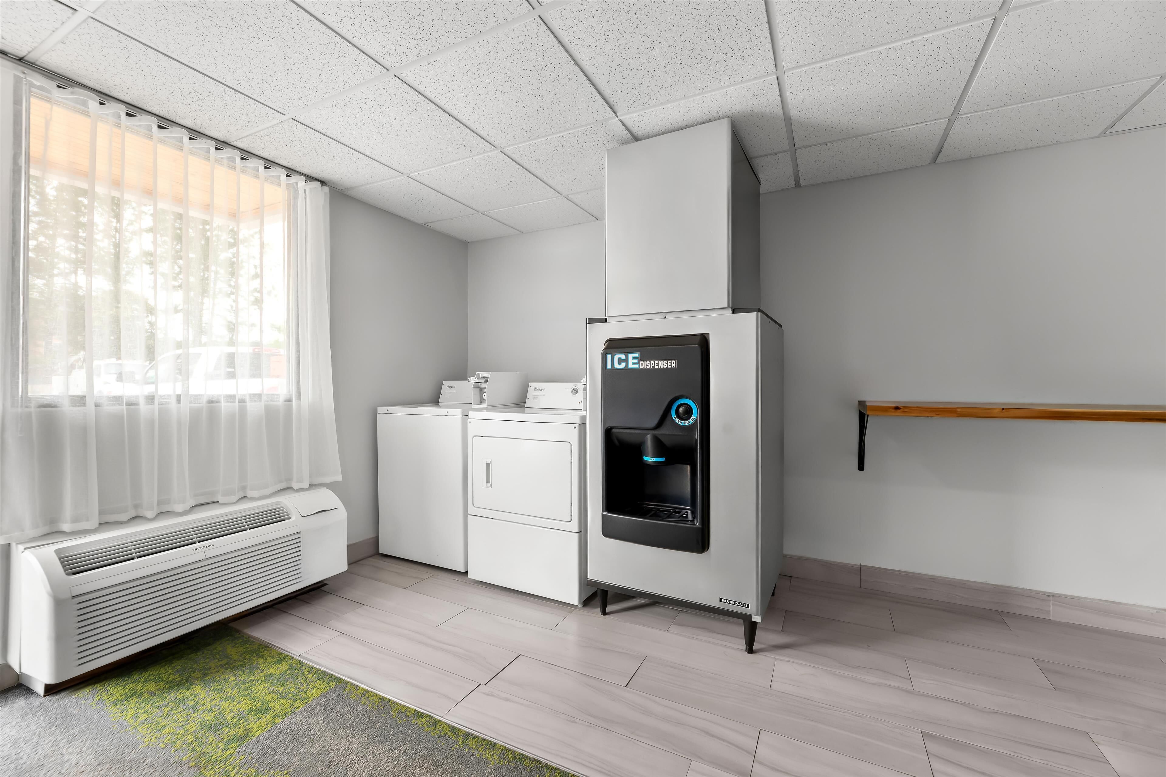 A modern hotel room with a built-in air conditioner, a water dispenser, a washing machine, and a wooden shelf.
