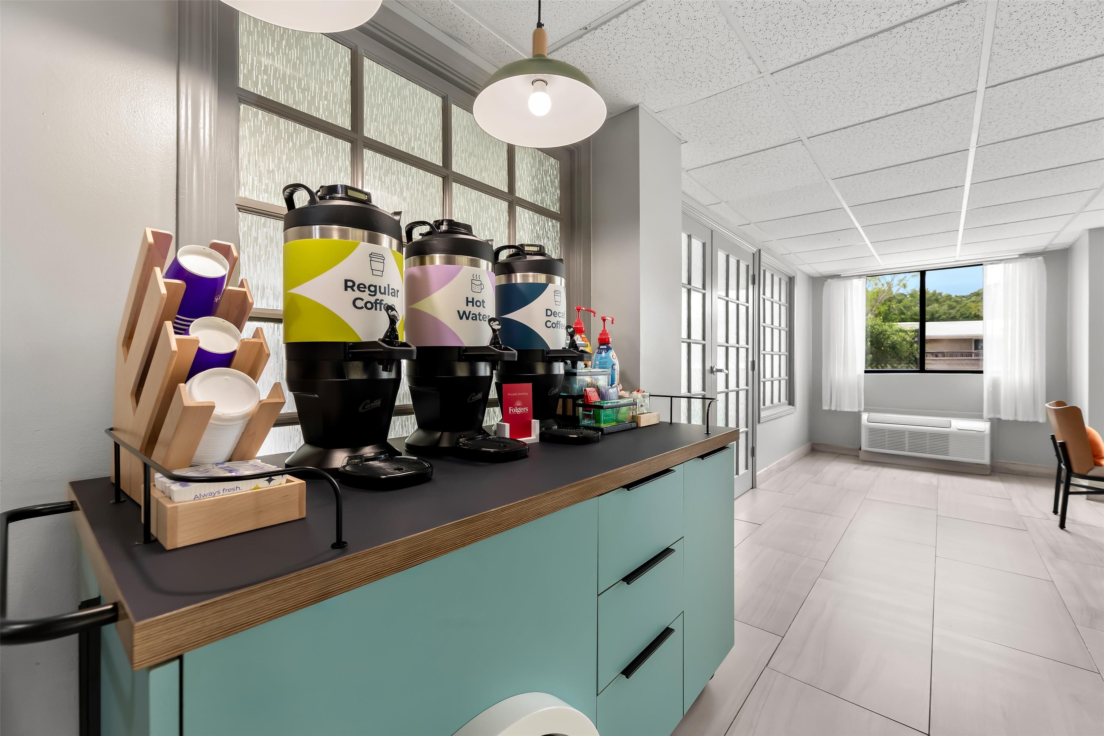 A modern kitchen area with coffee makers, a dish rack, and a window with a view of the outside.
