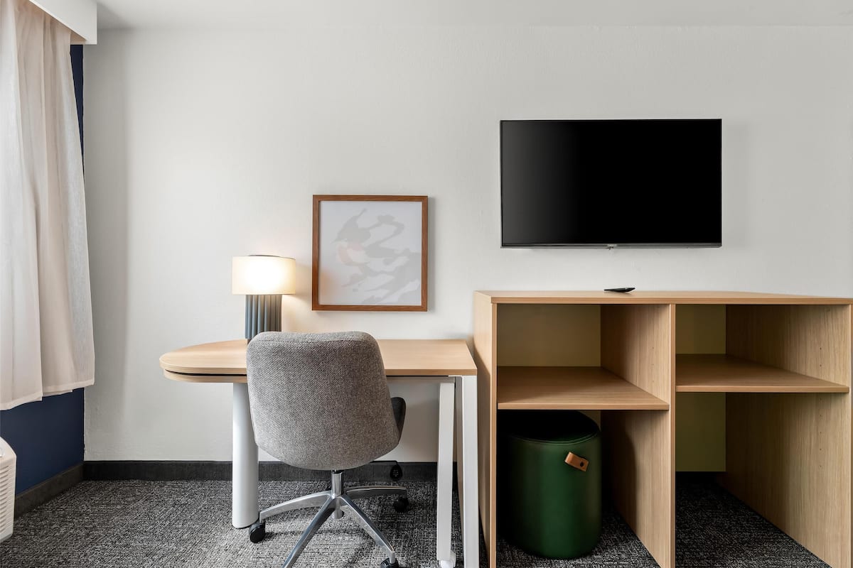 Een hotelkamer met een bureau, stoel, lamp, televisie en een ingelijst beeld aan de muur.
