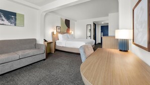 Una habitación de hotel con sofá, cama, escritorio y lámpara.