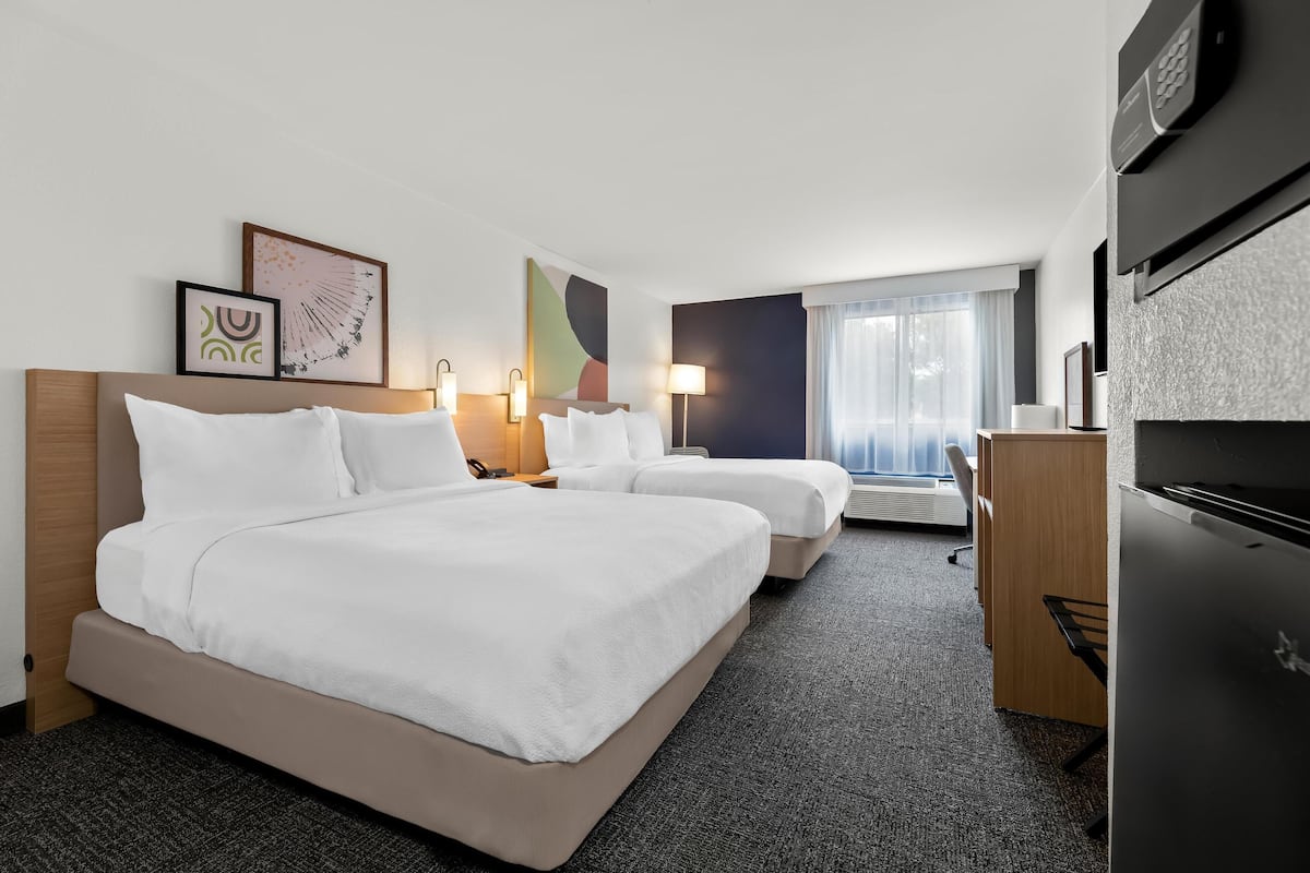 Een hotelkamer met twee bedden, een bureau, een koelkast en kunstwerken aan de muur.