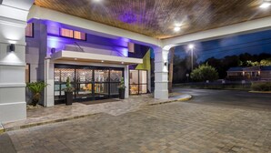 Una entrada de hotel moderna con un vestíbulo techado, un área de recepción y un espacio exterior ajardinado.