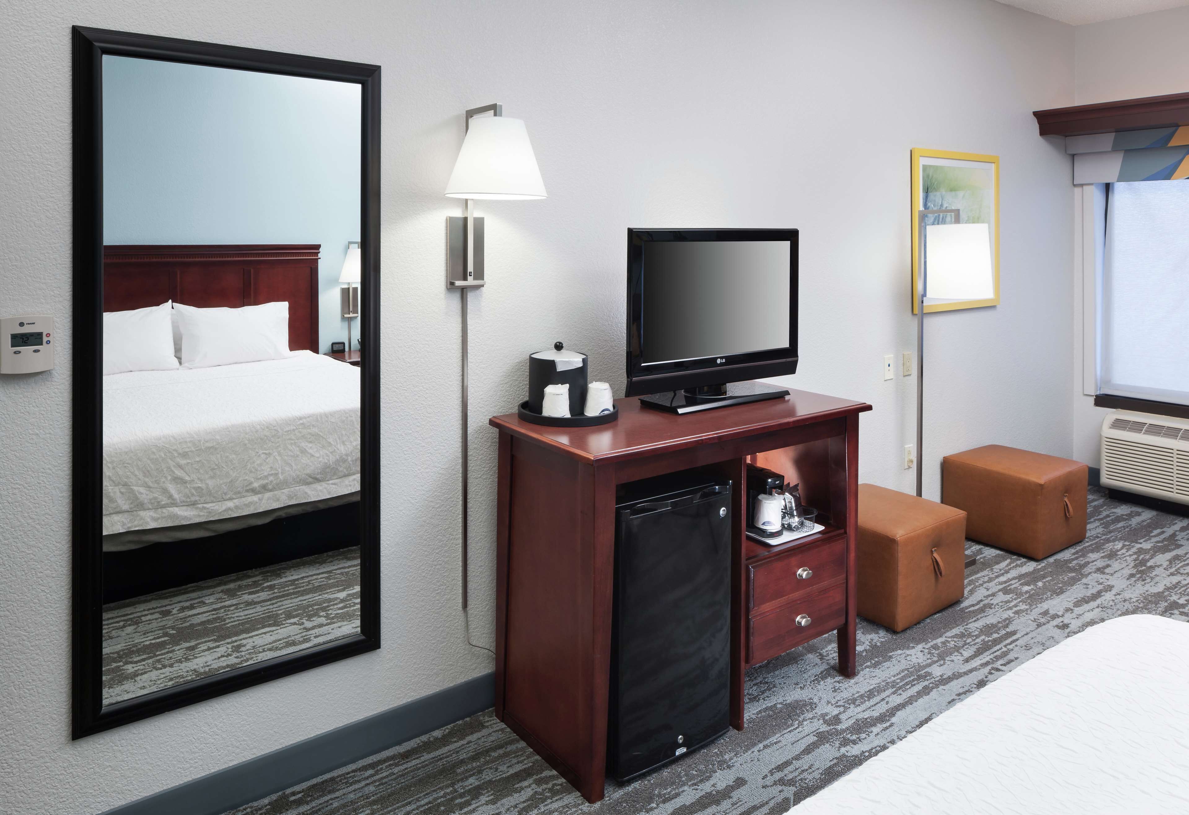 A hotel room with a bed, a desk with a television, a lamp, a mini-fridge, and a small seating area.