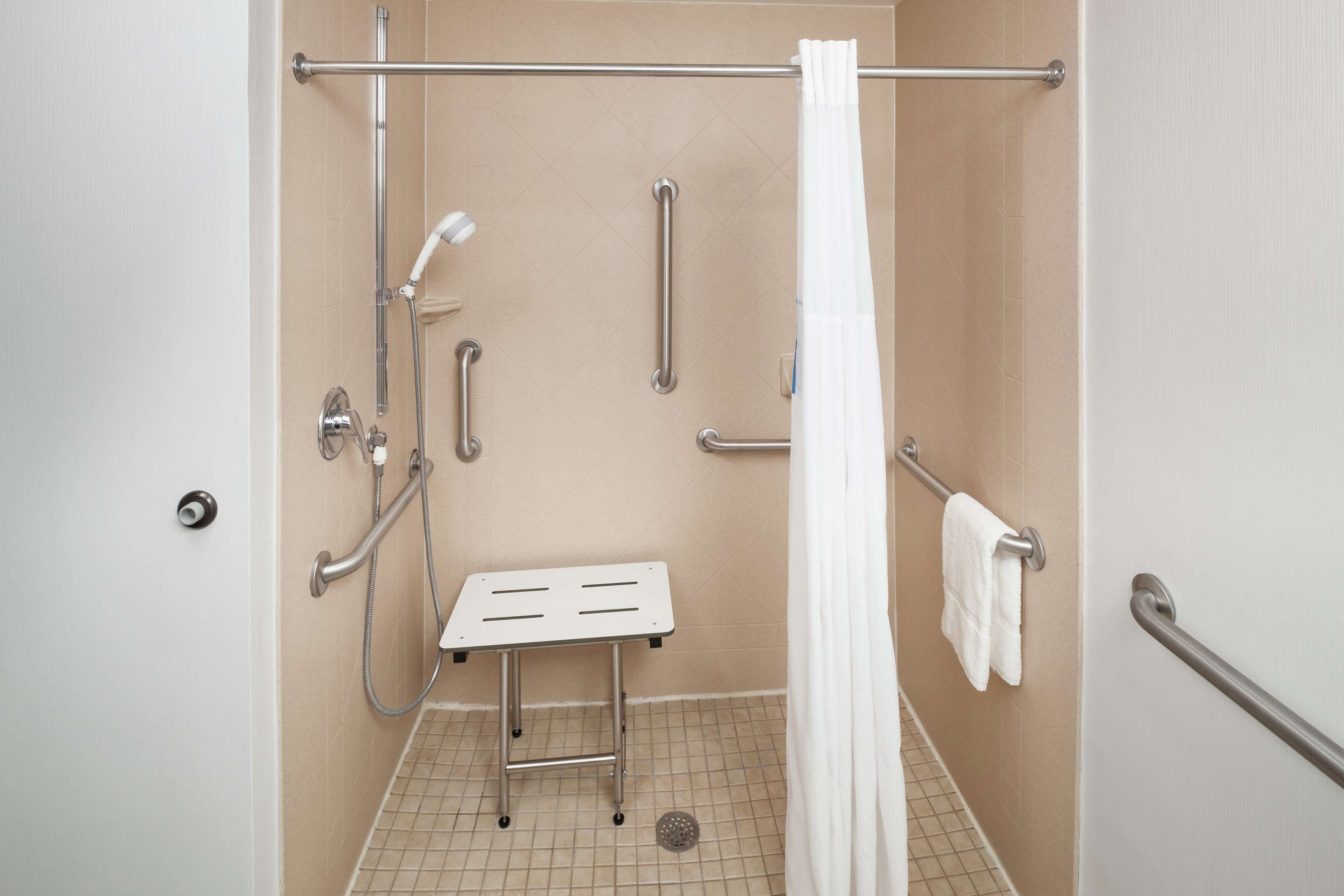 A handicap-accessible shower with grab bars, a shower seat, and a white shower curtain.