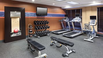 Un gimnasio con cintas de correr, mancuernas, un banco y un espejo grande.