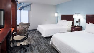 A hotel room with two beds, a desk with a chair, a television, and a lamp.