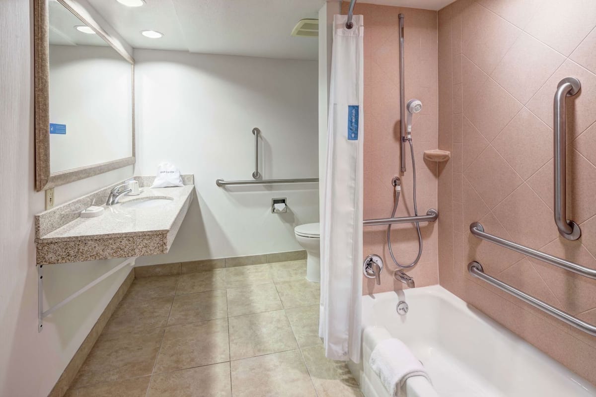 A bathroom with a sink, toilet, shower, and grab bars.