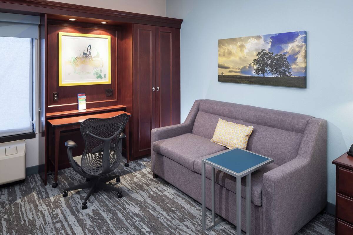 A room with a desk, office chair, couch, and a small table.