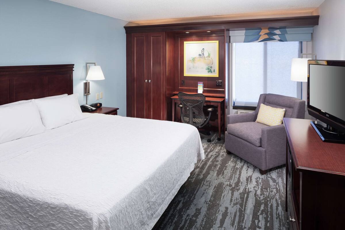A hotel room with a large bed, a desk with a chair, a television, and a window with a view.