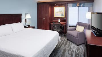 A hotel room with a large bed, a desk with a chair, a television, and a window with a view.