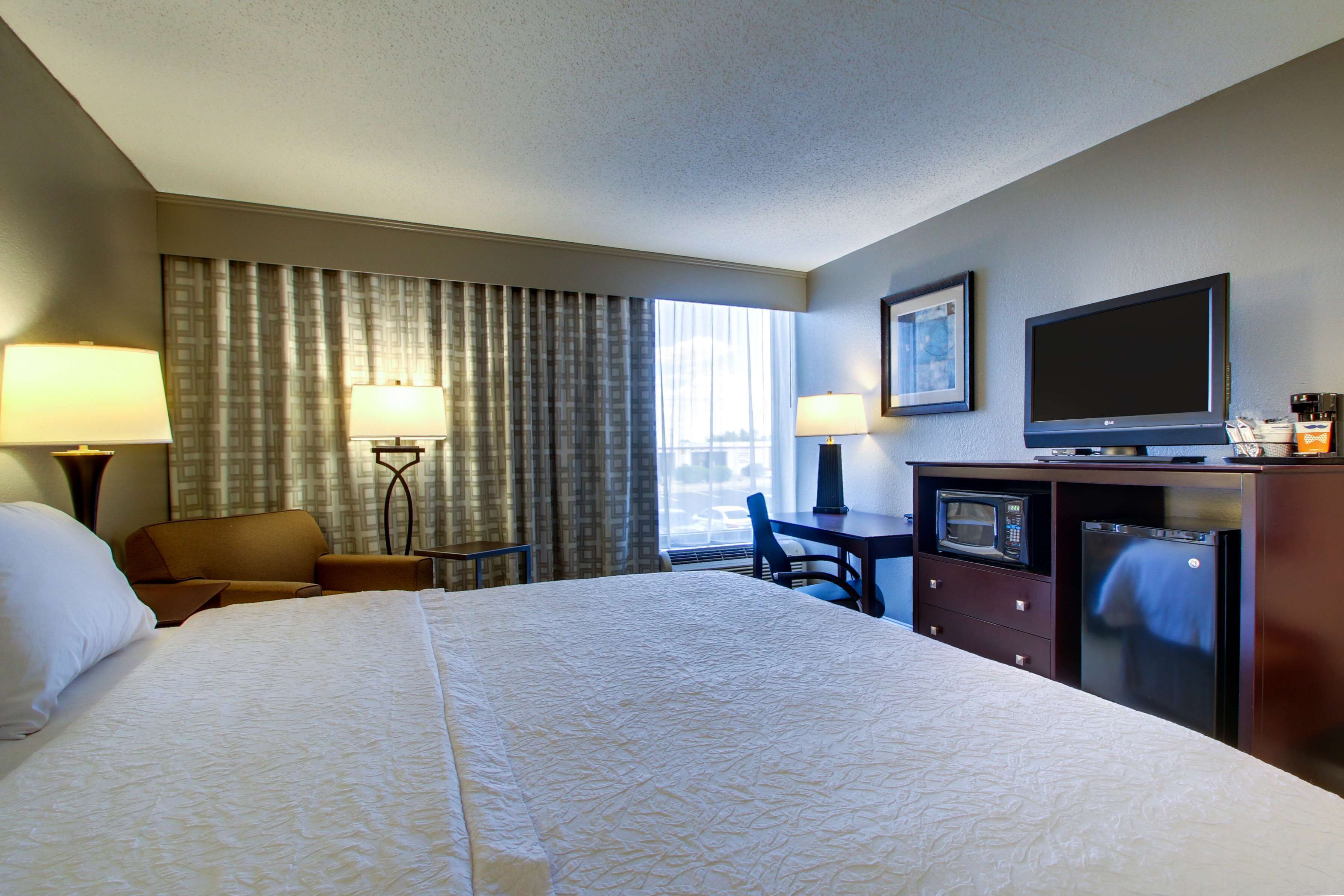 A hotel room with a large bed, a desk, a television, a microwave, and a refrigerator.