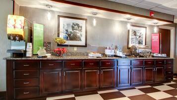 A hotel reception area with a checkered floor, a juice dispenser, a refrigerator, and a coffee machine.