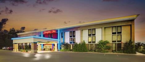 A hotel with a prominent "Hampton Inn" sign, a covered entrance, and a parking lot.