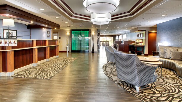 A hotel lobby with a reception desk, seating area, and a green glass door.