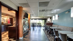 A hotel lobby with a checkered floor, a reception desk, a seating area with tables and chairs, and a large window providing natural light.