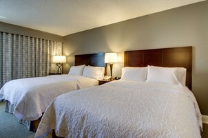 Habitación de hotel con dos camas, cada una con cubrecama blanco, cabecero de madera, lámparas de noche y teléfono en la mesita de noche.