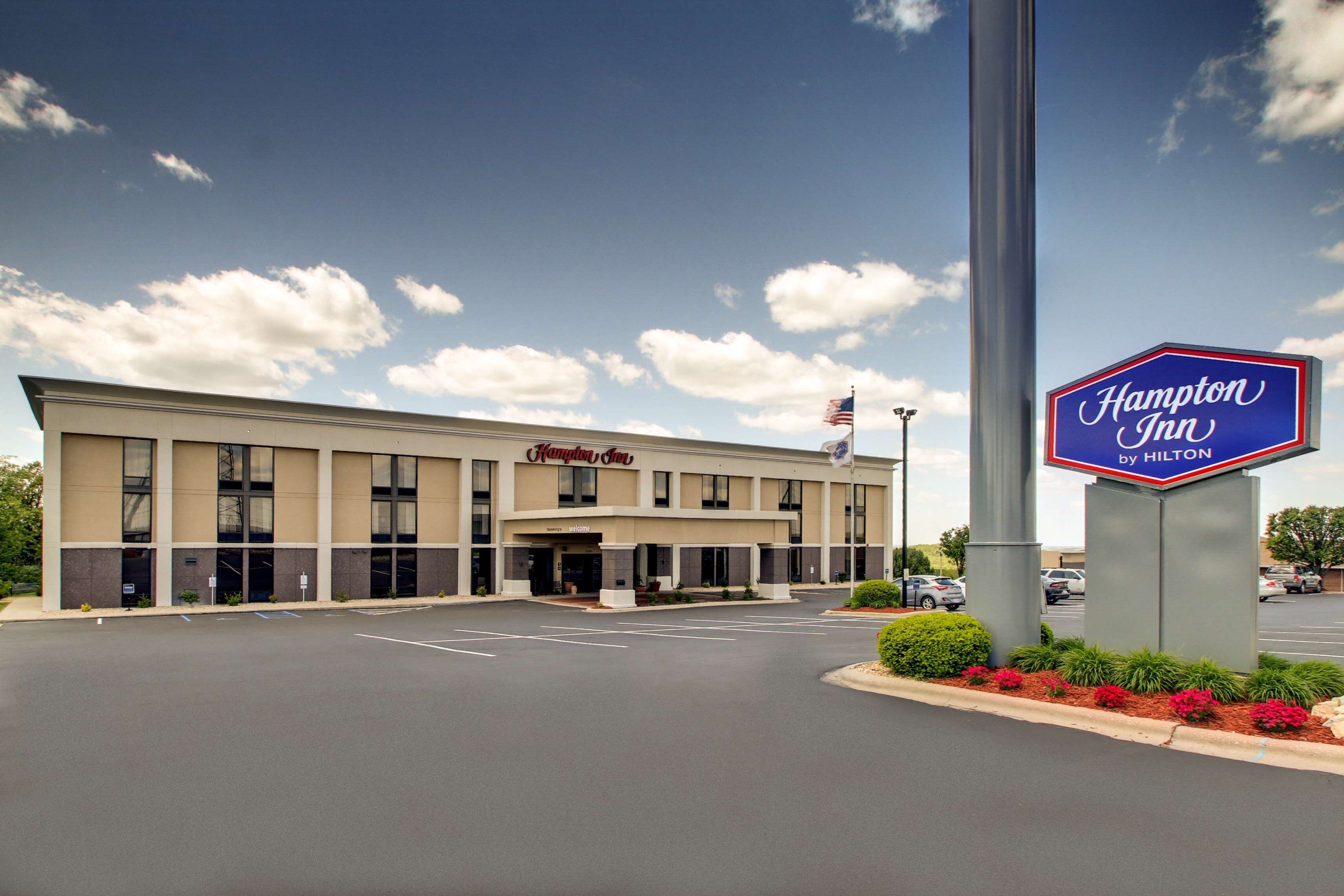 Ein Hampton Inn by Hilton Hotel mit Parkplatz und blauem Himmel.