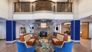 A spacious lobby with a fireplace, two blue armchairs, a wooden coffee table, and a high ceiling with a balcony. - Holiday Inn Express Hotel & Suites Bozeman West by IHG (Bozeman)