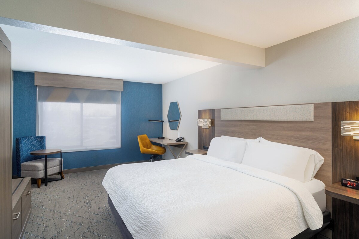 Quarto de hotel com uma cama grande, uma escrivaninha, uma cadeira e uma janela.