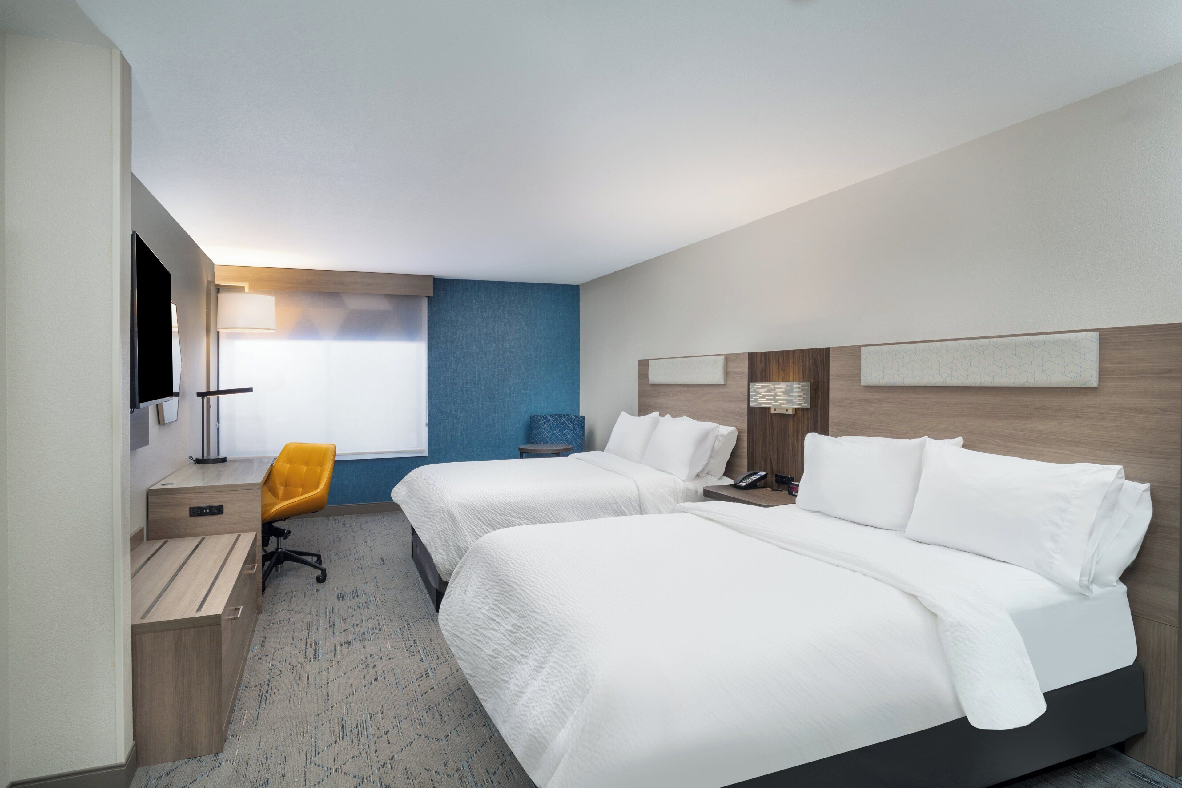 Ein Hotelzimmer mit zwei Betten, einem Schreibtisch, einem Stuhl, einer Lampe und einem Fenster.