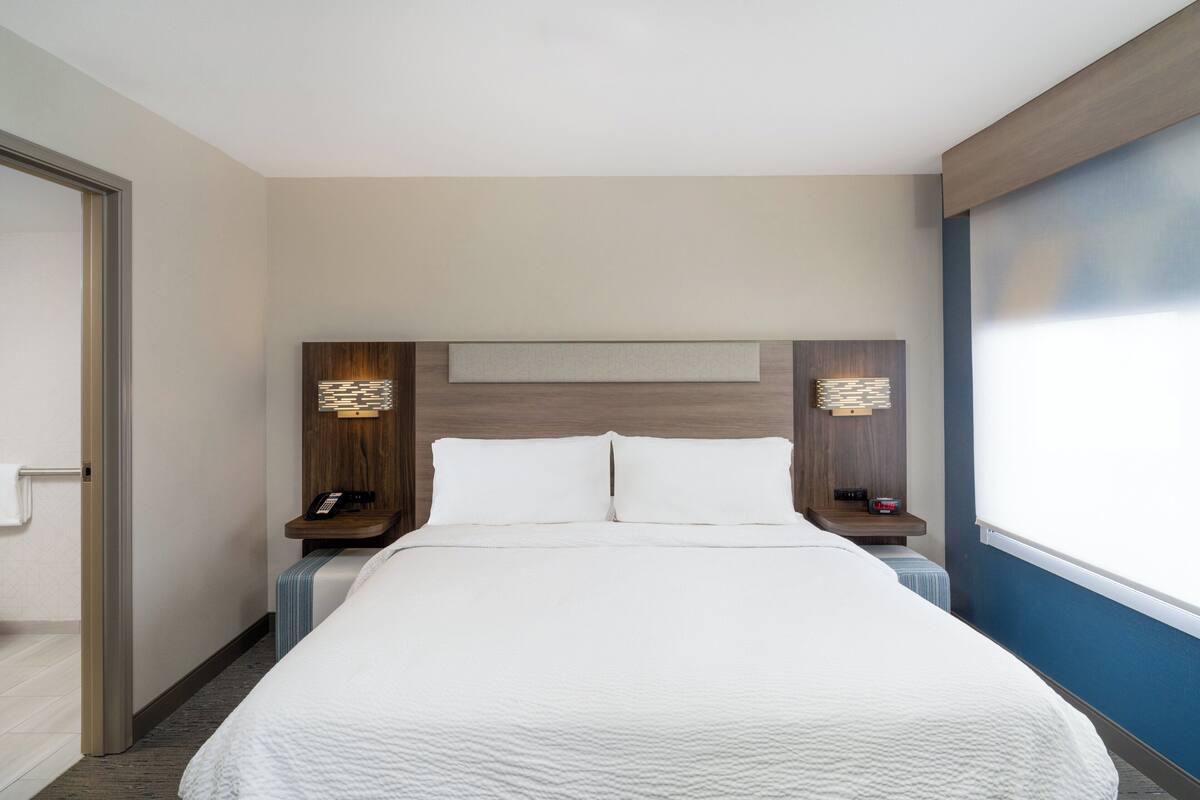 A hotel room with a large bed, bedside tables, a nightstand, a wall-mounted telephone, and a window.
