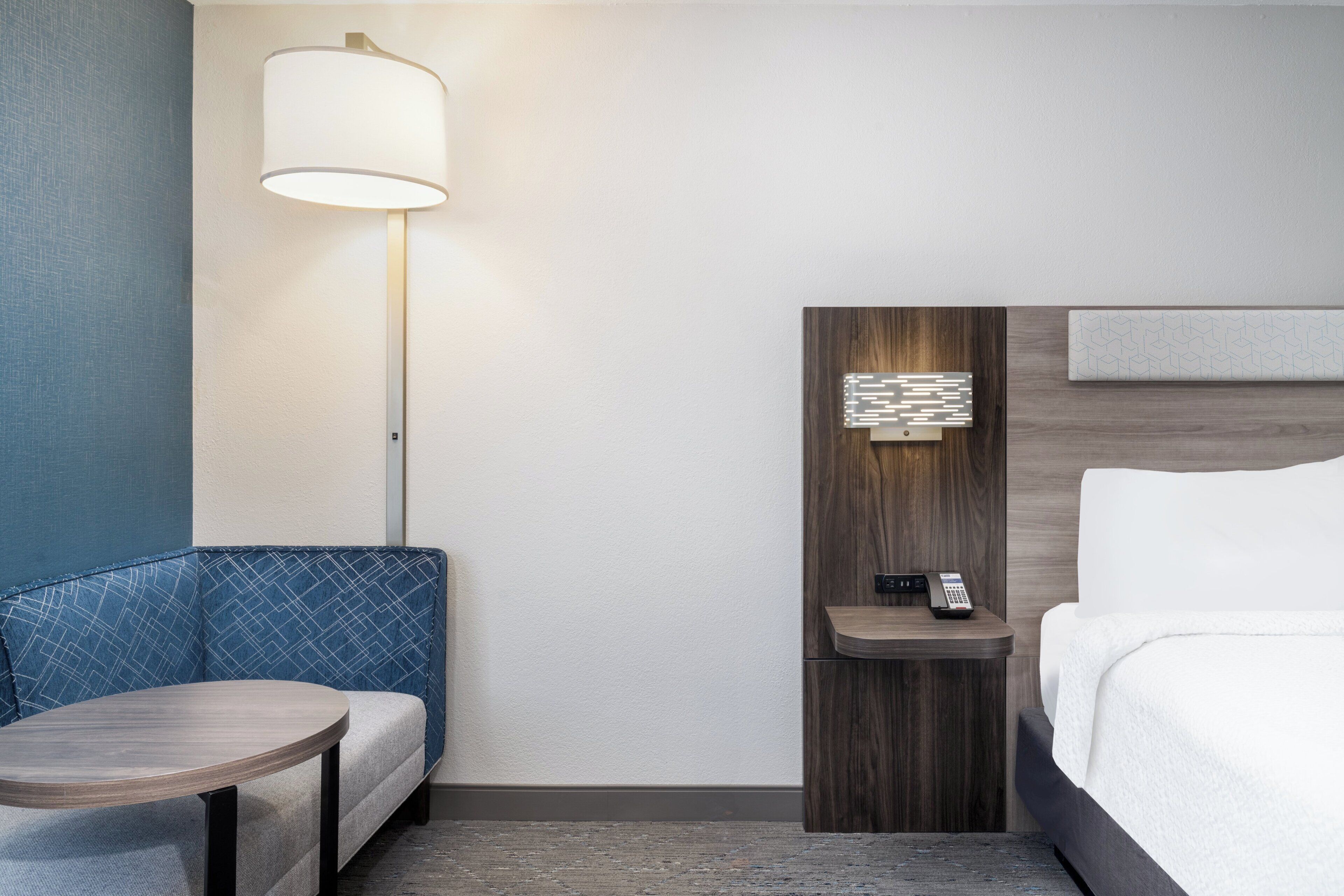 A hotel room with a bed, a desk, a chair, a lamp, and a wall-mounted phone.
