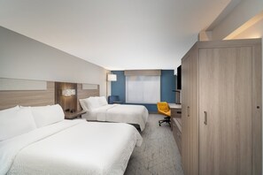 Quarto de hotel com duas camas, uma escrivaninha, uma cadeira, uma televisão e um guarda-roupa.