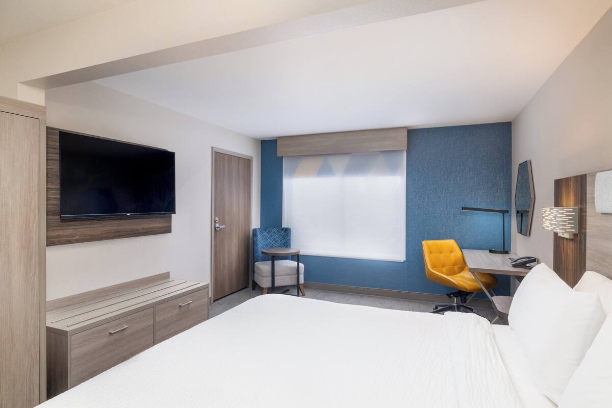 A hotel room with a bed, a desk, a chair, a television, and a wardrobe.