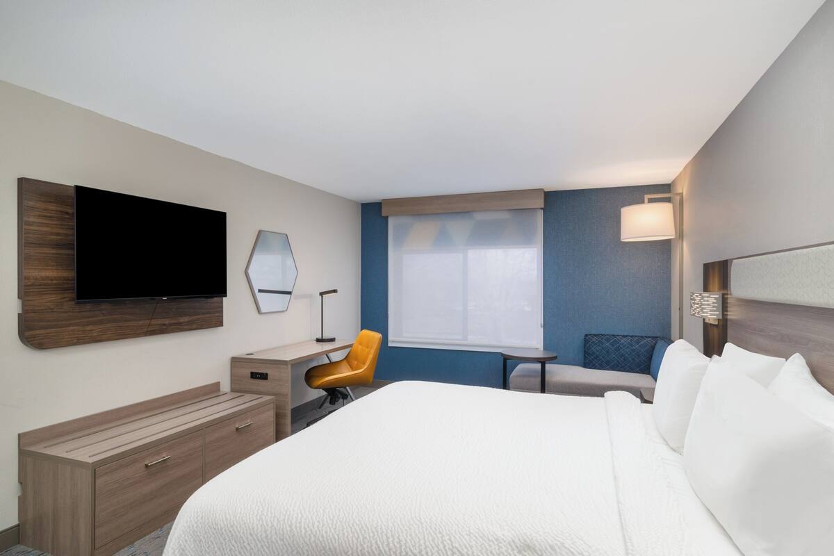 A hotel room with a bed, a desk, a chair, a television, and a window.