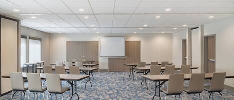 A conference room with a large screen, multiple tables, and chairs arranged for meetings.