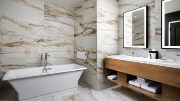 A modern bathroom with a freestanding bathtub, a wooden vanity, and marble walls.