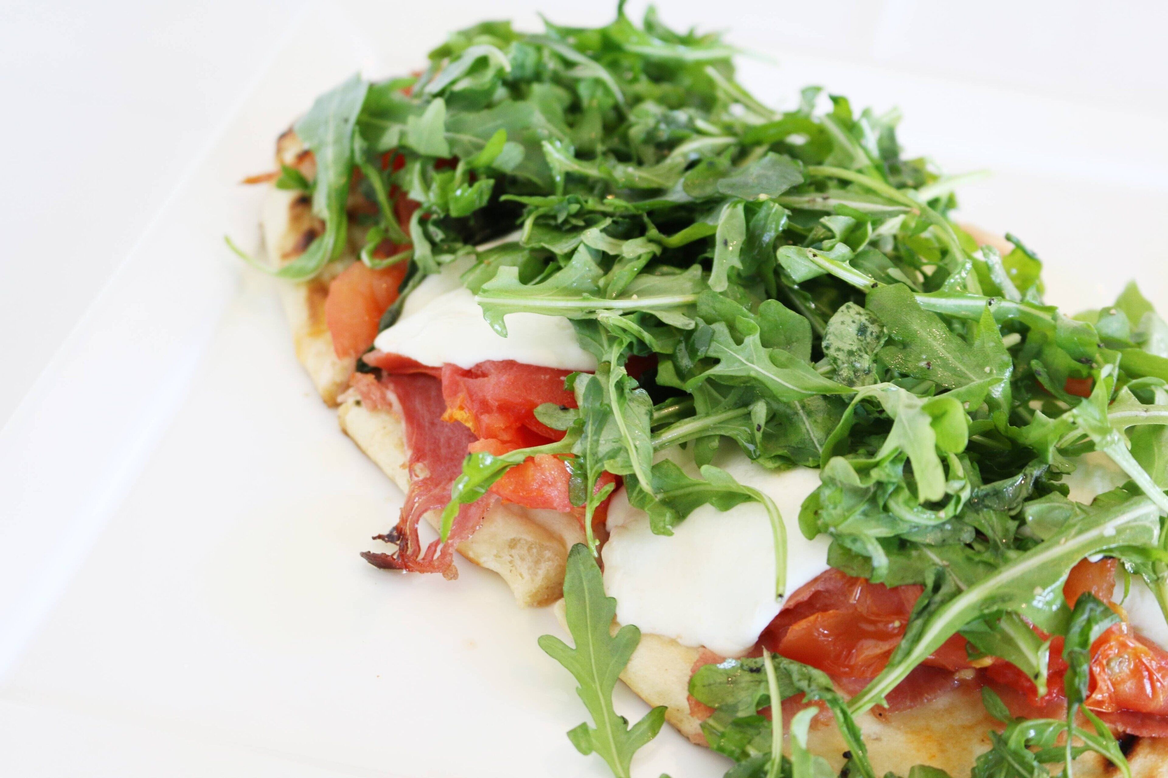 Un primo piano di un piatto con rucola, pomodoro e formaggio su un piatto bianco.