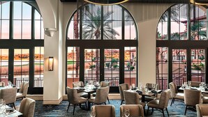 A restaurant with large arched windows, tables set for dining, and a view of the outdoors.
