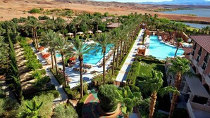 A resort with a central swimming pool, palm trees, and a view of a desert landscape with mountains.